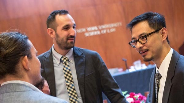 Three people in suits, including S. Matthew Liao (Director of the NYU Center for Bioethics and Master of Arts in Bioethics Professor), engage in conversation at New York University School of Law.