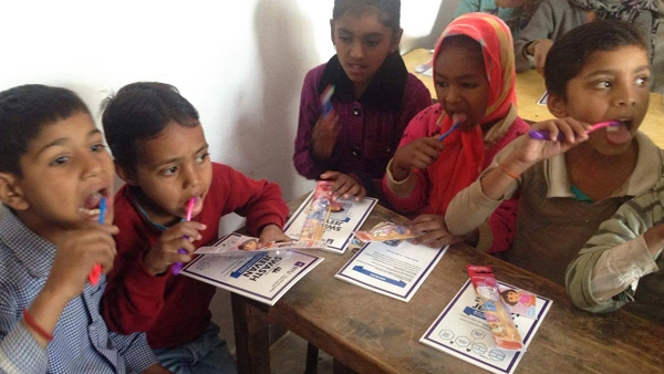 Five children sit around a small table while brushing their teeth.