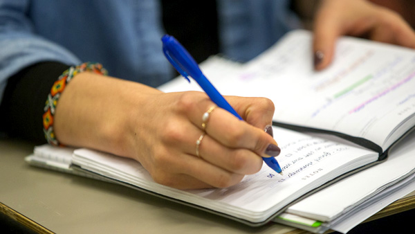 A close-up of a public health master’s degree student’s hand using a pen to take notes in a notebook.